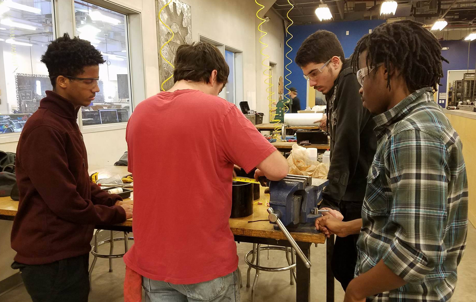 Photo of four students standing a work table with a caption of "Gashaw Bizana (far left), Alek Cook (center left), Alessandro Laspina  (center right) and Wakhile Shongwe (far right) working on manufacturing of the team’s prototype design of the auger. Photo courtesy of Next Level Devils"