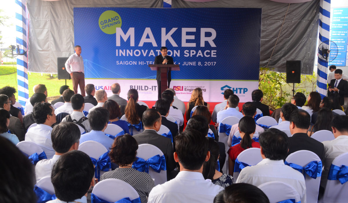 Photo of two men on a stage in front of a crowd. Caption is Le Hoai Quoc, president of the Saigon Hi-Tech Park, welcomes guests to the Maker Innovation Space at the June 8 launch in Ho Chi Minh City, Vietnam. Photo courtesy of BUILD-IT