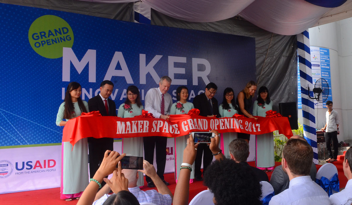 Photo of nine people behind a red ribbon that say Maker Space Grand Opening 2017. Caption is "U.S. Ambassador to Vietnam Ted Osius (fourth from right) leads the ceremonial ribbon cutting with Tran Nam Tu (second from left), vice director general, Department of Science and Technology, Ministry of Education and training, Le Hoai Quoc (fourth from right), and Mary Tarnowka (second from right), U.S. consul general. Photographer: Quynh Giao"
