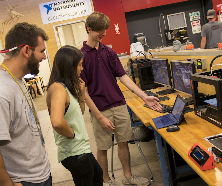 Photo of three students standing in front of a laptop computer with a caption of "Patrick Hull (right) shows off his design of the drill exhaust escape and drill tether to Brittany Nez (center) and Christian Sclafani (left). Photographer: Marco-Alexis Chaira/ASU"