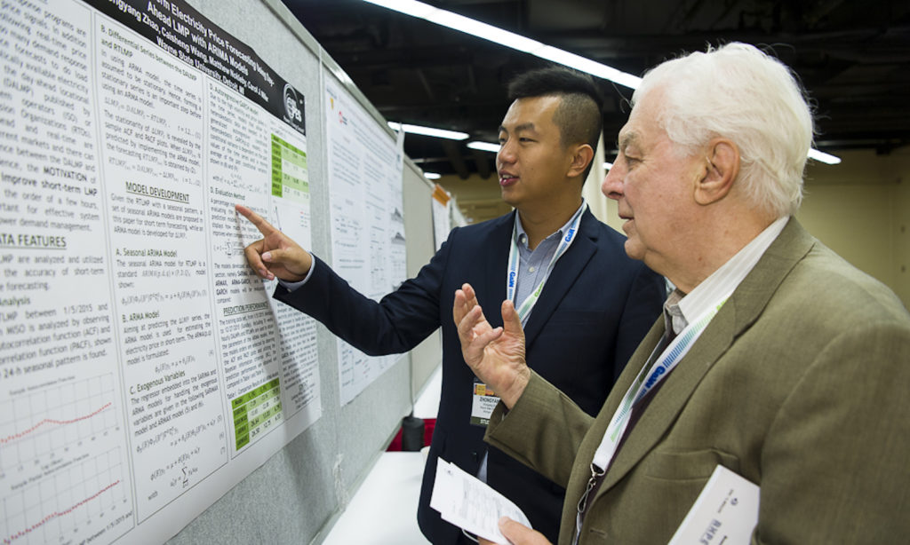 Photo of two men looking at a poster. Caption: George Karady representing the U.S.-Pakistan Centers for Advanced Energy USPCAS-E and ASU, surveys posters at the IEEE PES 2017 General Meeting . Photo credit: IEEE PES