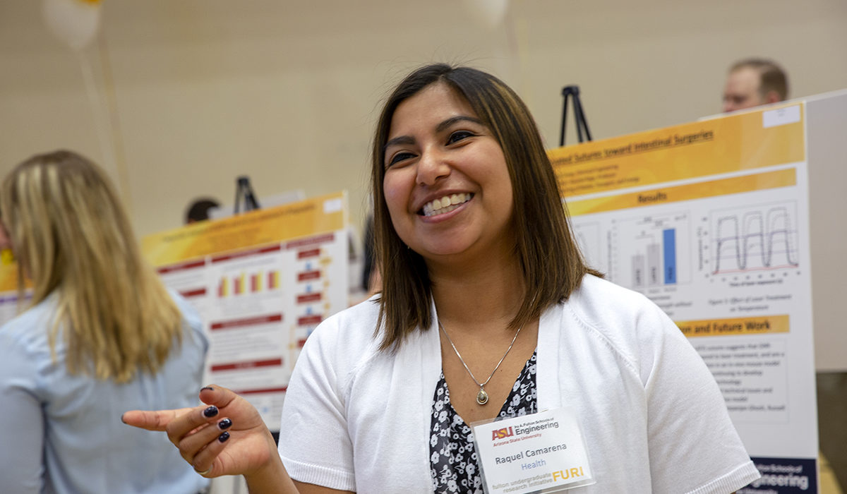 Photo of a girl smiling in front of a poster. Caption: Raquel Camarena, a graduate student in industrial engineering, explains her master’s thesis project on improving the identification and treatment of Alzheimer’s Disease at the FURI Symposium. The hands-on experience with operations research helped her land a full-time job with Raytheon after graduation. Photographer: Jessica Hochreiter/ASU