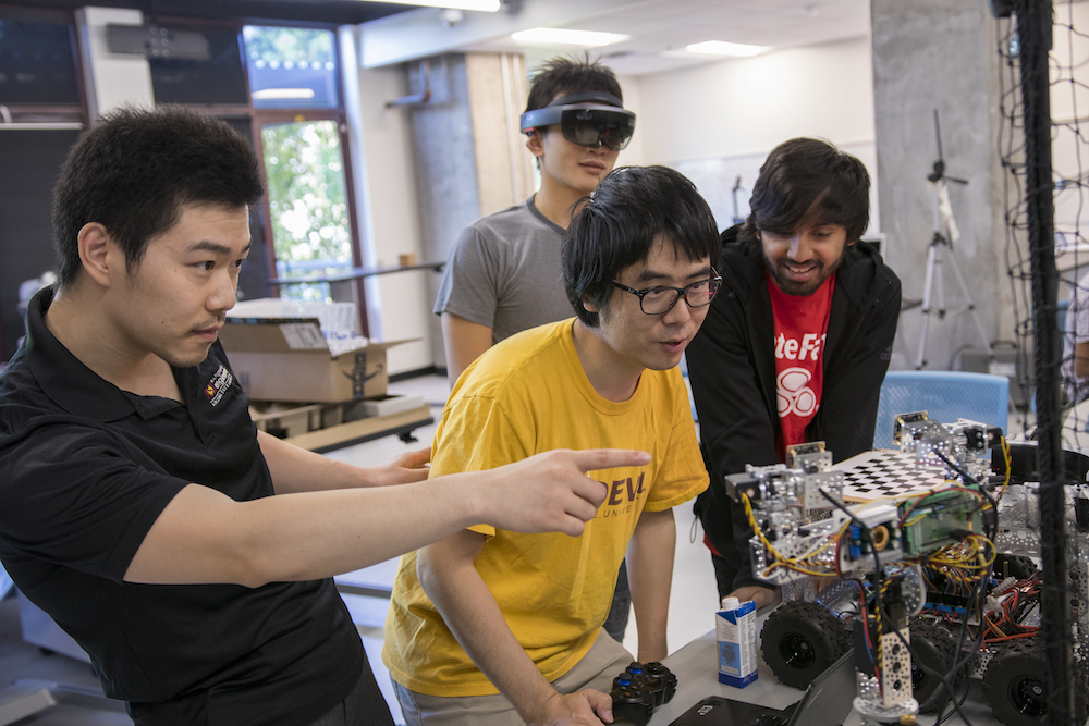 Four men (one in virtual reality glasses) looking at a drone