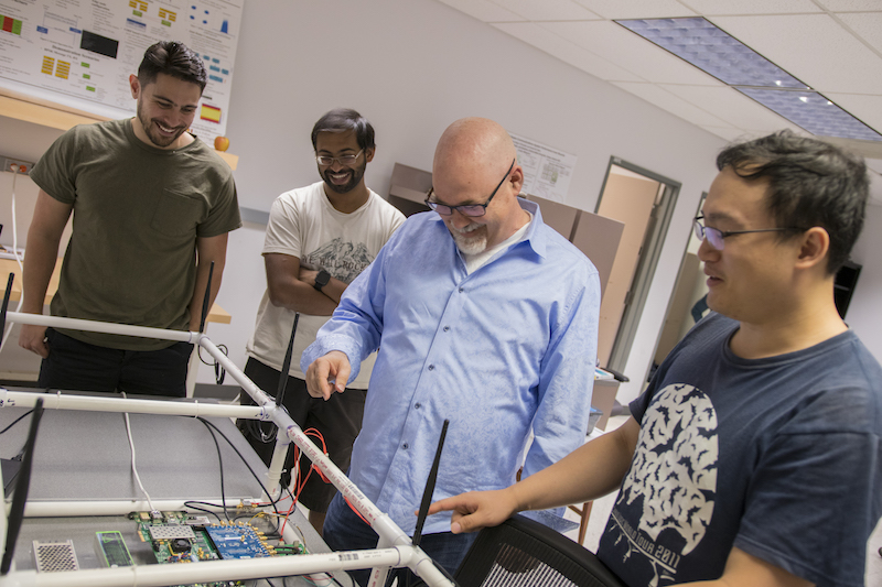 professor Bliss and three students looking at something on a table
