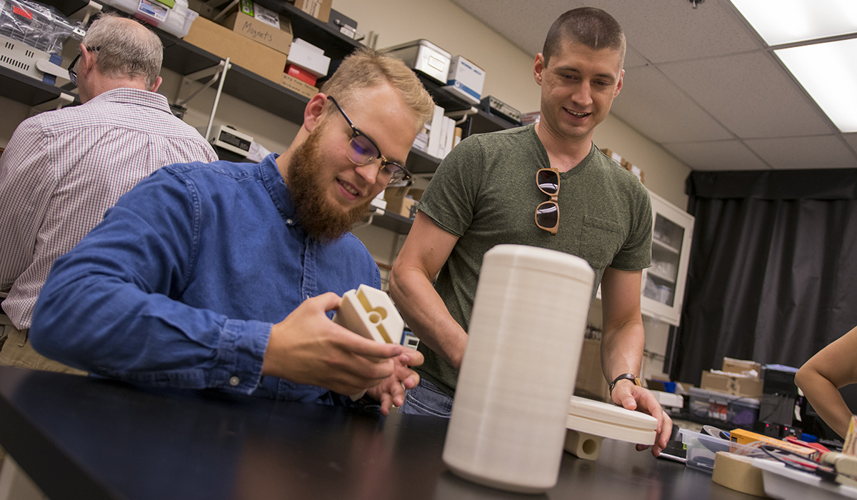 one student sitting and looking at object, one student standing