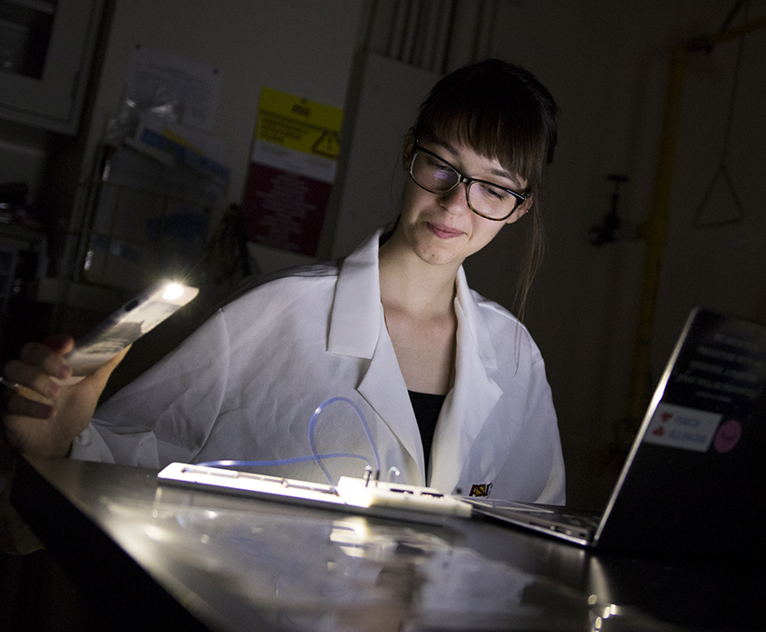 student holding a light illuminating object on table