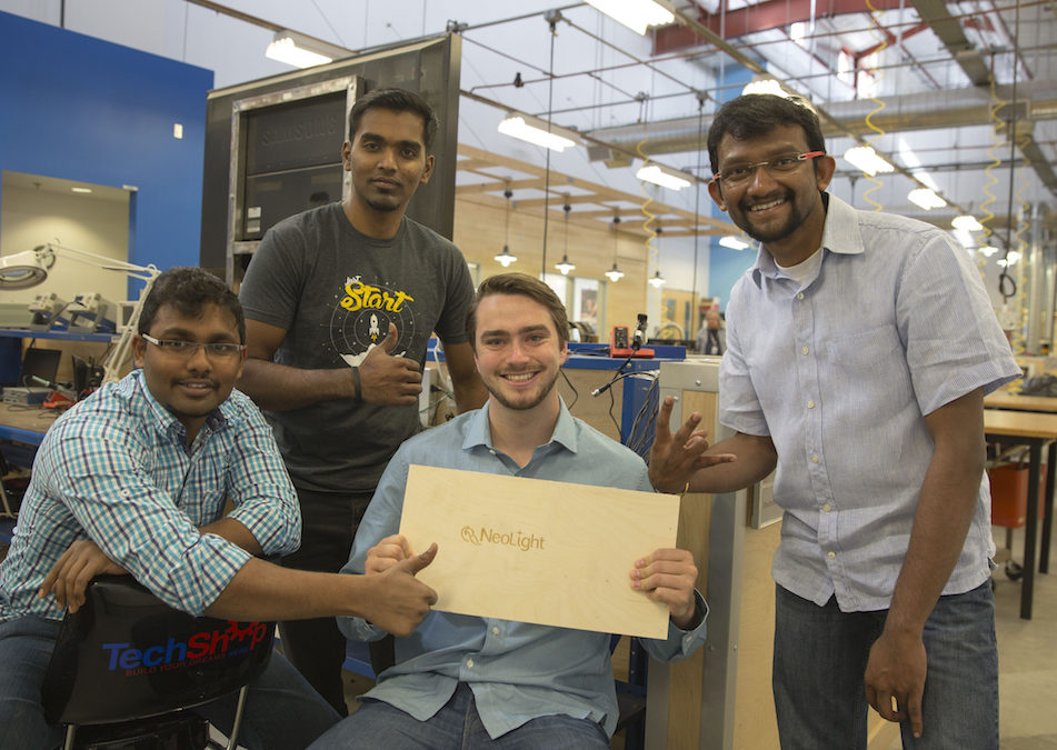 four students holding a piece of wood that says NeoLight