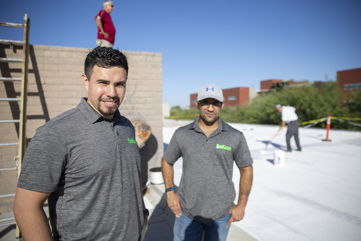 Two men standing in front of others applying coating to rooftop