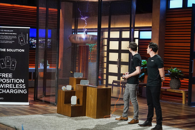 two men standing next to a Tesla coil