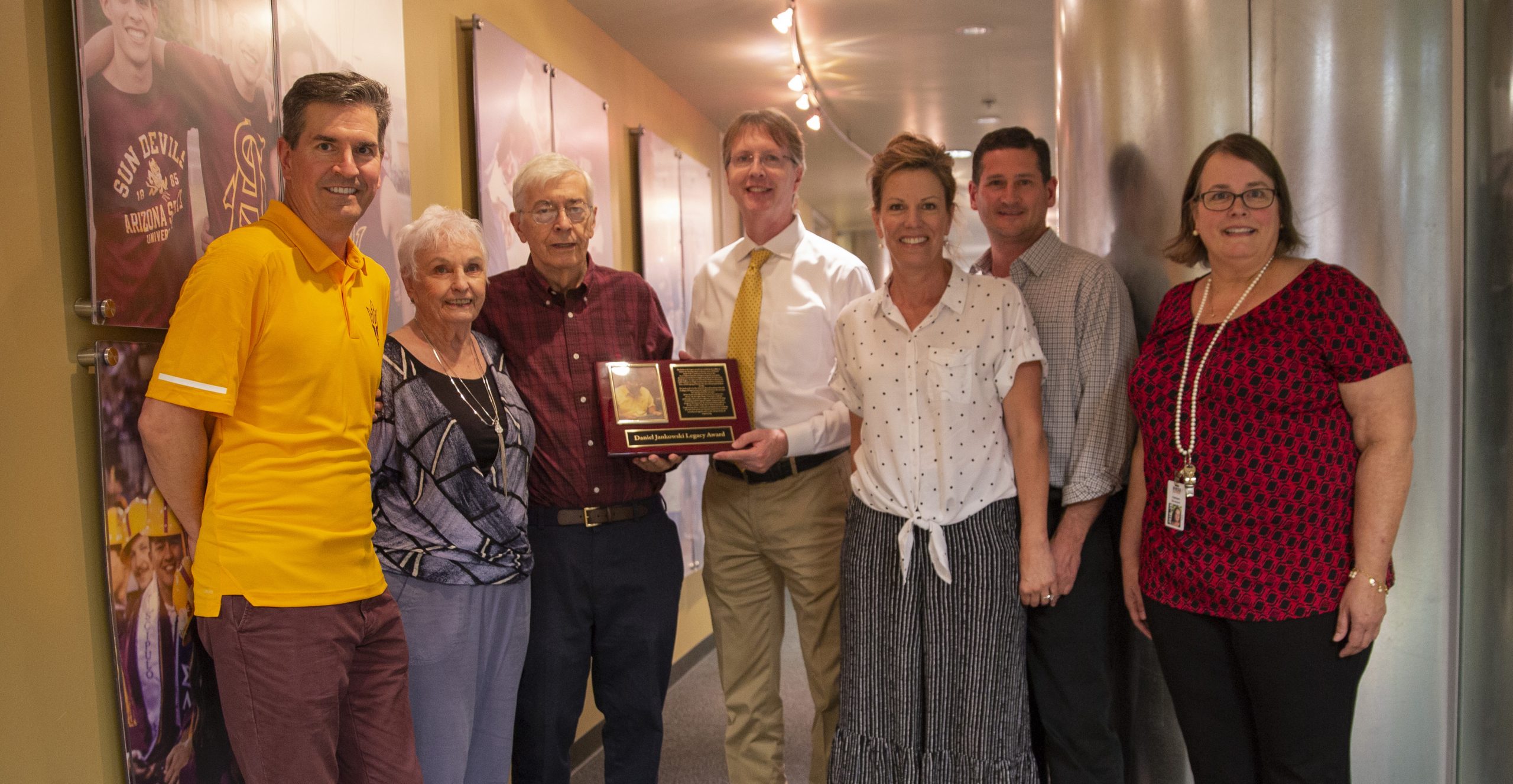 Photo of seven people in a hallway posing with a Jankowski Legacy Award plaque