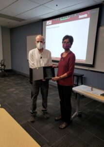 Director Stephen Phillips hands Chaitali Chakrabarti stands next to Director Stephen Phillips as he hands her he glass award in a box.