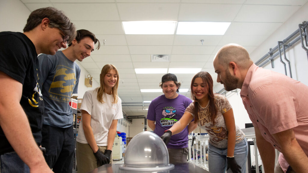 A group of Swift Coat engineers and interns looks at a prototype of a spacesuit helmet that uses the company’s anti-fog coating.